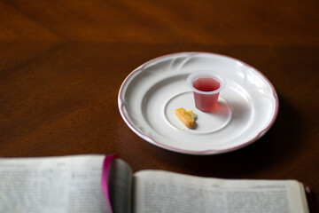 Christian Holy Communion sacraments, wine and bread with open Holy Bible, on a wood table.