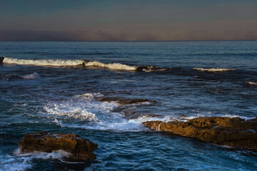 Fototapeta na wymiar 2022-03-20 LA JOLLA SHORE LINE WITH WAVES AND ROCKS AND A BLURRY CLOUD BANK IN THE DISTANCE