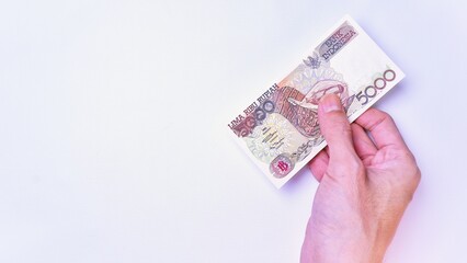 Indonesian Rupiah the official currency of Indonesia. Man's hand is making a payment. Male hand showing Indonesian Rupiah Note. Business Investment Economy and Finance Concept Uang 5000 5.000 Rupiah
