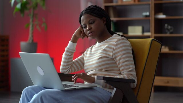 Bored African American Woman Sit In Armchair At Home Office Unable To Concentrate On Work At Laptop. Tired Exhausted Girl Student Feel Unmotivated To Study. Freelancer Irritated With Monotonous Job