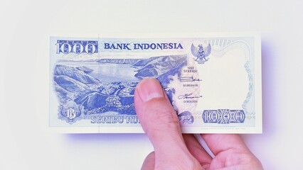 Indonesian Rupiah the official currency of Indonesia. Male hand showing Indonesian Rupiah note. Business Investment Economy Money and Finance Concept Uang 1000 Rupiah Kuno Vintage and ancient concept.