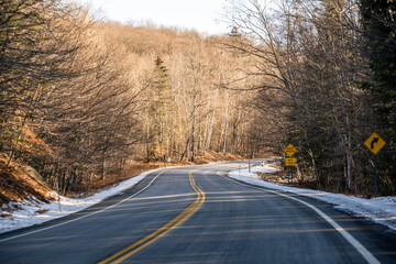 Fototapeta premium Winding road with snow on the roadside in a bare winter forest in northern New Hampshire