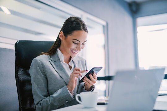 A happy female entrepreneur scrolling on phone in modern office.