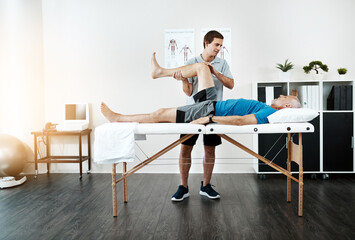 We are going one step at a time. Shot of a young male physiotherapist helping a client with leg exercises whos lying on a bed.