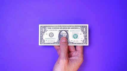 Businessman's hand holding American Dollar Banknotes, isolated on a purple background. Business Investment Economy Saving Loan Income Money and Finance concept. One Dollar, 1 USD. Prosperity concept.