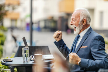 An old businessman in a suit the cafeteria cheering for the good news on the laptop. 