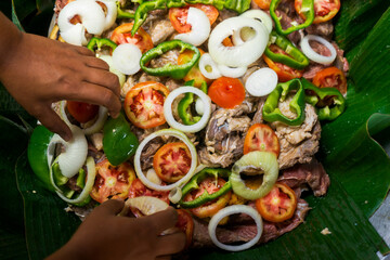 Closeup of the hands of a latin woman preparing the traditional Nicaraguan food known as Vaho. A steam-based preparation of beef, vegetables such as cassava, tomato and onion cooked in a large pot