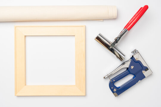 Tools for stretching a canvas with a photo on a wooden stretcher. Square stretcher, canvas roll, tongs and a gun for staples on a white background, top view