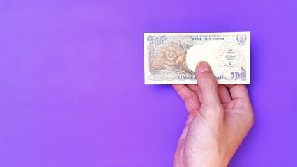 Indonesian Rupiah the official currency of Indonesia. Man's hand is making a payment. Male hand showing Indonesian Rupiah note. Business Investment Economy Money and Finance Concept. Uang 500 Rupiah