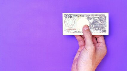 Indonesian Rupiah the official currency of Indonesia. Man's hand is making a payment. Male hand showing Indonesian Rupiah note. Business Investment Economy Money and Finance Concept. Uang 500 Rupiah