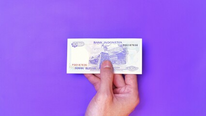 Indonesian Rupiah the official currency of Indonesia. Man's hand is making a payment. Male hand showing Indonesian Rupiah note. Business Investment Economy Money and Finance Concept. Uang 1000 Rupiah