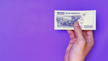 Indonesian Rupiah the official currency of Indonesia. Man's hand is making a payment. Male hand showing Indonesian Rupiah note. Business Investment Economy Money and Finance Concept. Uang 1000 Rupiah