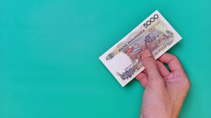 Indonesian Rupiah the official currency of Indonesia. Man's hand is making a payment. Male hand showing Indonesian Rupiah note. Business Investment Economy and Finance concept. Uang 5000 5.000 Rupiah
