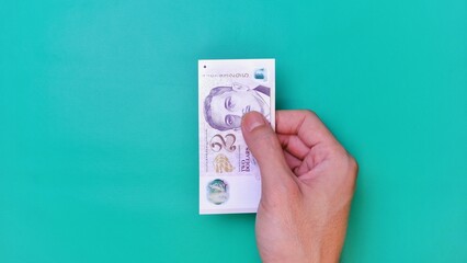 Singapore Dollar is the official currency of Singapore. Business Investment Economy Money Income Loan and Finance concept. Businessman's hand showing Singapore Dollar on a green background. 2 SGD.