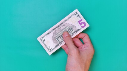 Man's hand is making a payment. Business Investment Economy Money Loan Saving Income and Finance concept. Male hand showing dollar bills on green background. Five Dollar. 5 USD. Prosperity concept.