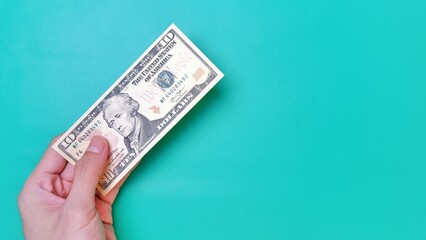 Man's hand is making a payment. Business Investment Economy Money Loan Saving Income and Finance concept. Male hand showing dollar bills on green background. Ten Dollar. 10 USD. Prosperity concept.