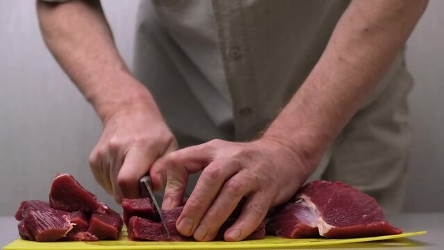 slicing and preparing raw meat for further cooking of steaks, barbecue or minced meat. close-up of the hands of a male chef slicing fresh raw meat fillet into pieces with a knife. slow motion.