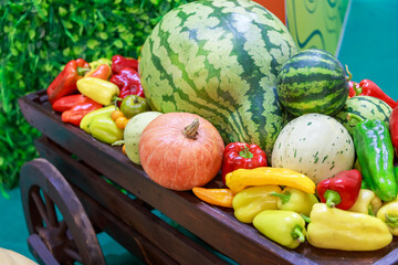 Concept abundance of vegetables and fruits. Natural food. Harvest in a garden wooden wheelbarrow, wooden cart with watermelons, pumpkins, peppers