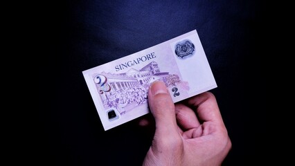 Singapore Dollar is the official currency of Singapore. Business Investment Economy Money Income Loan and Finance concept. Businessman's hand showing Singapore Dollar on a black background. 2 SGD.
