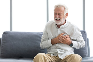 senior elderly man chest pain or suffering from heart attack on a sofa