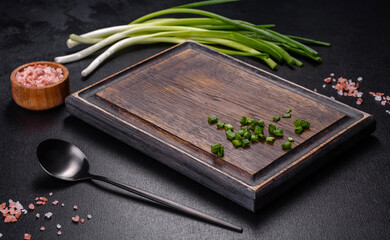 Black metal spoon and rectangular cutting board on black concrete background