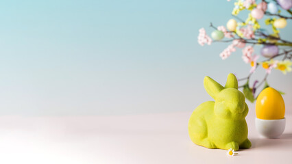 Easter banner with a yellow egg and a green rabbit on a blue background with a branch of flowers....