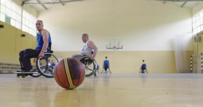 A person with a disability lifts a basketball from the ground while training in a modern hall