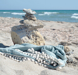 Muslin towel on the coast against the background of the sea. Organic body textiles and a tower of stones on a sandy beach.