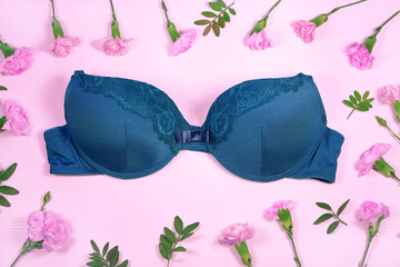 Beautiful blue bra surrounded by flowers, pink background, top view. Stylish lingerie, underwear.