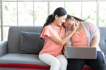young teenage girl using laptop computer and her mother embracing on sofa