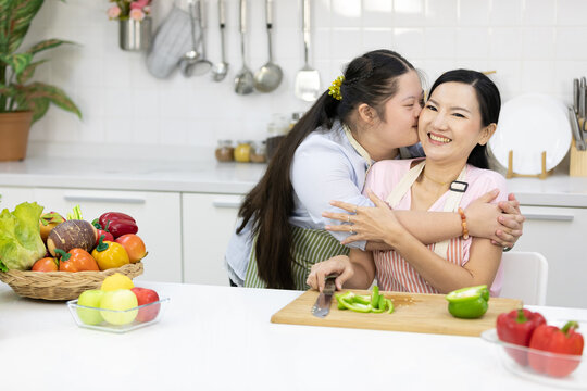 down syndrome teenage girl hugging and kissing her mother while cooking food in the kitchen