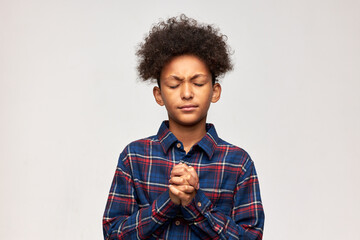Boy of dark ethnicity with clenched fists keeping eyes closed, trying to make wish, frowning,...