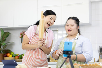 mother and down syndrome teenage girl or her daughter rolling out dough and live streaming online via smartphone on tripod in a kitchen