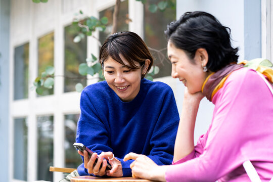 カフェテラスでスマートフォンを見るミドル世代の日本人女性2人