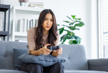 Asian young beautiful cheerful happy exciting female gamer model sitting on cozy couch smiling...