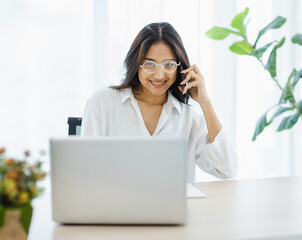 Asian young beautiful female university student wearing optical eyeglasses sitting at working desk remotely studying learning streaming online via laptop notebook computer at home during quarantine