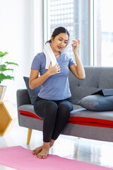 Asian young pretty happy healthy female athlete sport girl in casual sporty outfit sitting smiling on sofa holding using white towel cleaning drying sweat relaxing resting after exercising online