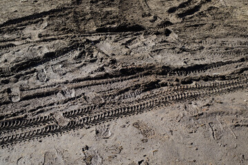 Wet dirt, footprints and tire marks on muddy road outdoors. Texture surface of countryside land