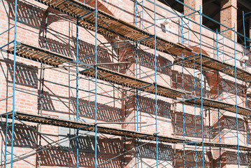 Reconstruction and restoration of red brick building, scaffolding at facade of old wall, outdoor construction