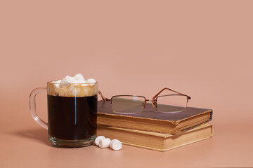 A glass cup of coffee with marshmallows, stack of old books and glasses