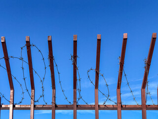 Metal fence with barbed wire on its top against blue sky