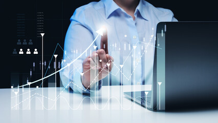  woman sits at a laptop in front of a holographic chart with growing indicators. Business...