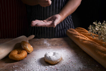 Baker decorates sweet donut on wooden table.
