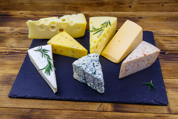 Set of various types of cheese on black slate board on a wooden table
