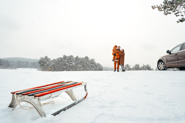 Sledge against happy family on a walk in winter forest