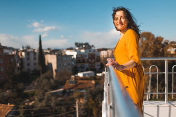 A girl in a yellow dress stands on a balcony during a strong wind