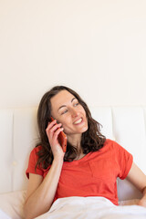 A woman sits on a bed and calling on the phone