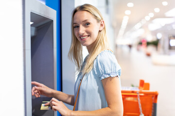 young woman stands on against atm in a shopping center