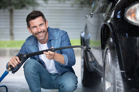 happy attractive man perfusing with water his silver car