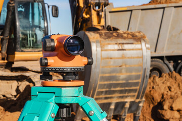 Level with an excavator in the background. Construction level or theodolite. Geodetic instruments and equipment for the construction and earthworks.